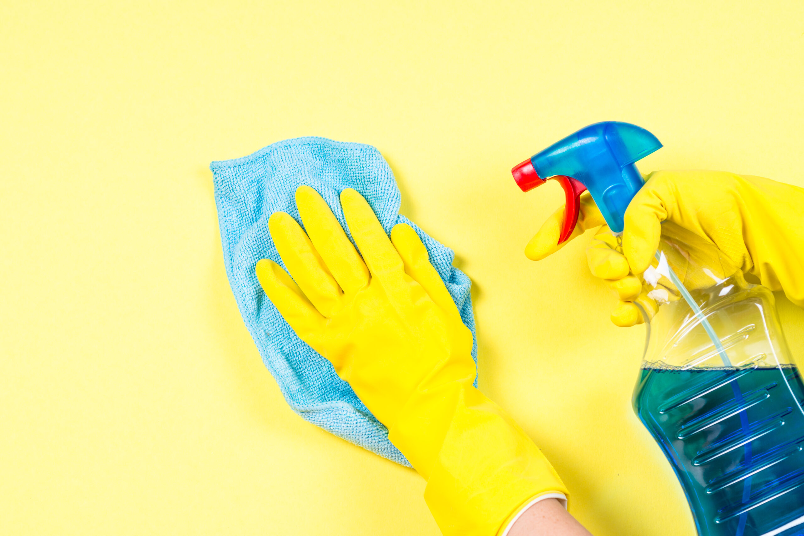 Woman cleaning yellow wall with microfiber rag, gloves and cleaning spray agent.